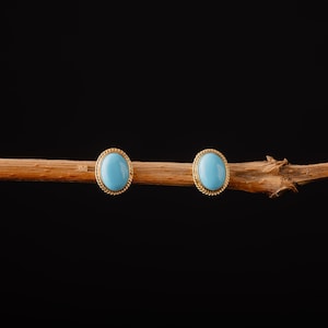 May include: A pair of gold earrings with oval-shaped turquoise stones.