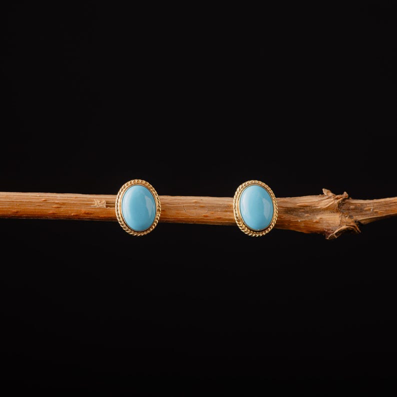 May include: A pair of gold earrings with oval-shaped turquoise stones.