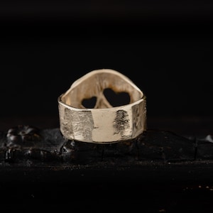Op de afbeelding: Zilveren ring met een getextureerde band en een ontwerp van twee harten aan de bovenkant. De ring ligt op een zwart oppervlak.