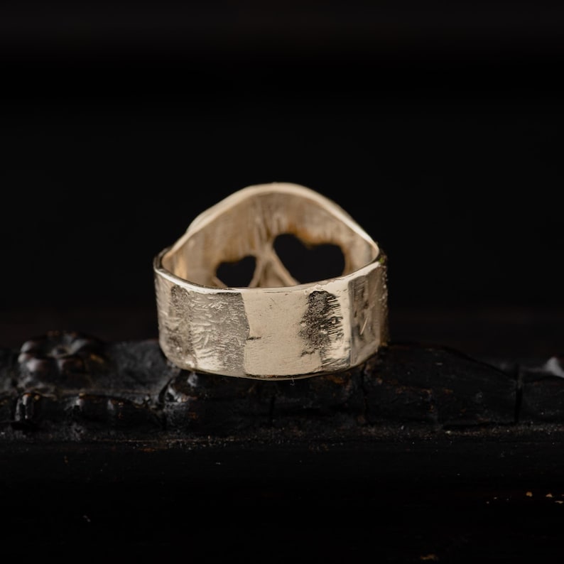Op de afbeelding: Zilveren ring met een getextureerde band en een ontwerp van twee harten aan de bovenkant. De ring ligt op een zwart oppervlak.
