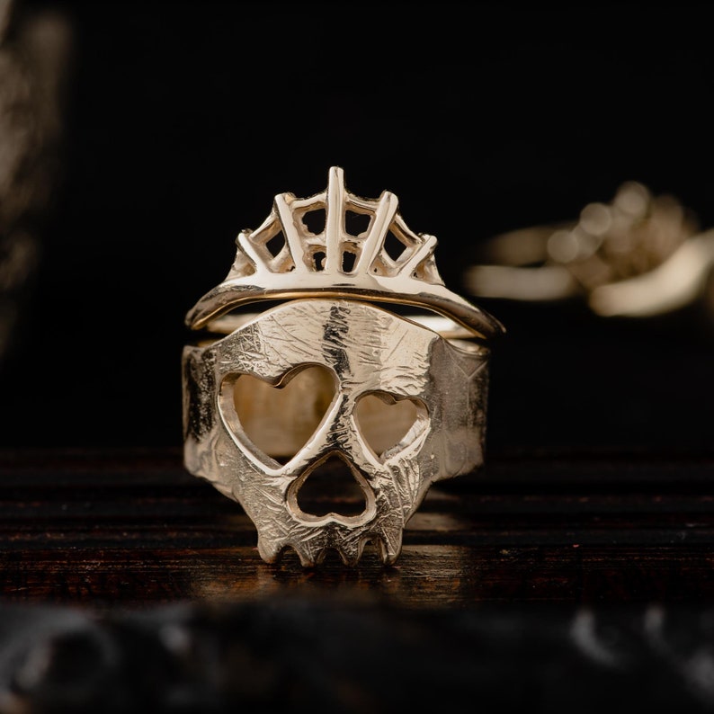 Op de afbeelding: Een gouden ring met een schedelontwerp en een kroon erop. De schedel heeft twee hartvormige oogkassen.