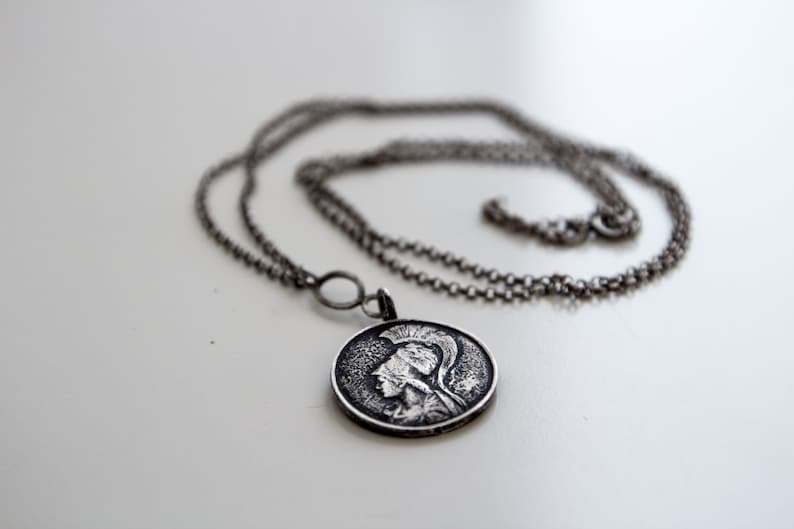 May include: A silver chain necklace with a round pendant featuring a detailed profile of a person wearing a helmet.