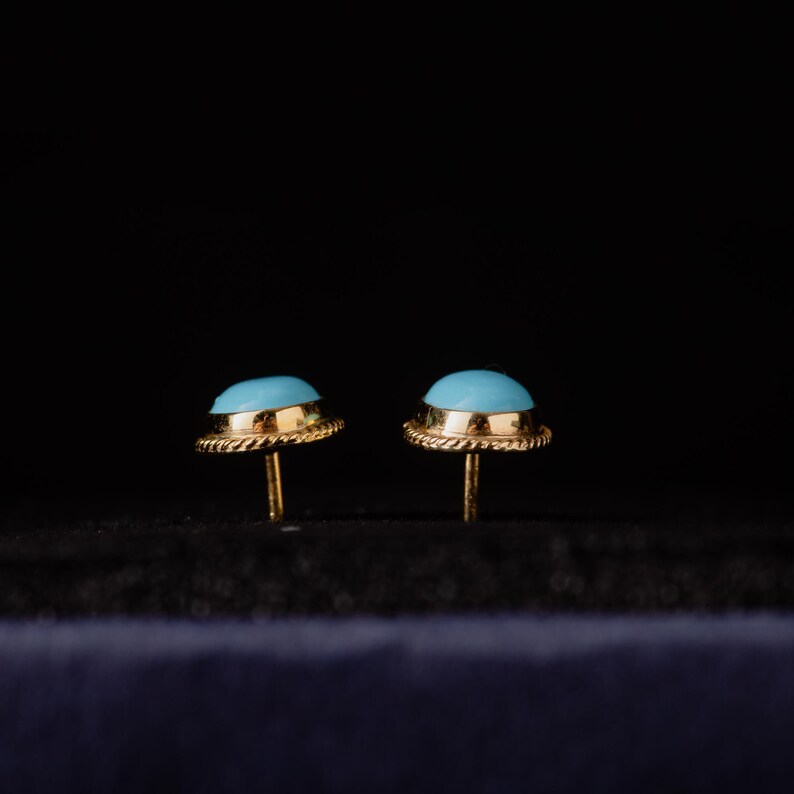 May include: A pair of gold earrings with blue turquoise stones. The earrings have a simple design with a round stone set in a gold bezel.