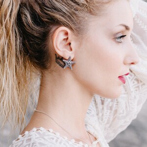 May include: A woman with blonde hair wearing a white lace top and a silver starfish earring.