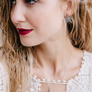 May include: A woman wearing a white lace top with a silver necklace and earrings featuring a starfish design.