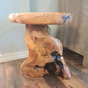 May include: A handcrafted wooden side table with a natural, organic design. The table features a round top and a uniquely shaped base, showcasing the wood's grain and knots. The table measures approximately 18 inches in height.