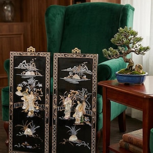 Puede incluir: Dos paneles de pared rectangulares negros con incrustaciones de nácar que representan figuras tradicionales, paisajes y flora. Cada panel tiene un colgador de metal dorado en la parte superior y un borde detallado.