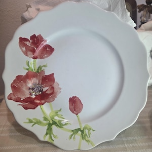 May include: White ceramic plate with a scalloped edge, featuring a watercolor design of red anemone flowers and green leaves. The plate has a smooth surface and a classic, elegant aesthetic, suitable for serving food.