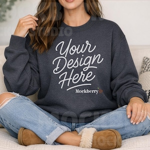 May include: Dark gray sweatshirt with the text "Your Design Here" in white script. The model is wearing light blue jeans with distressed knees and brown shearling slippers. The sweatshirt is a crew neck style.