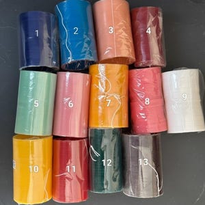 K&ouml;nnte beinhalten: Eine Sammlung von dreizehn Rollen dekorativen Bandes in verschiedenen Farben, darunter Marineblau, T&uuml;rkis, Pfirsich, Burgunderrot, Mintgr&uuml;n, Hellrosa, Orange, Koralle, Wei&szlig;, Gelb, Rot, Dunkelgr&uuml;n und Anthrazitgrau. Jede Rolle ist in klarem Kunststoff verpackt.