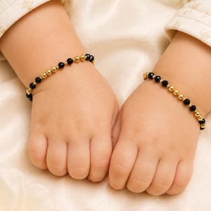 May include: A pair of bracelets featuring alternating small black beads and polished gold-tone spherical beads. The bracelets are designed with a repeating pattern of black and gold beads, creating a consistent look across both pieces of jewellery.