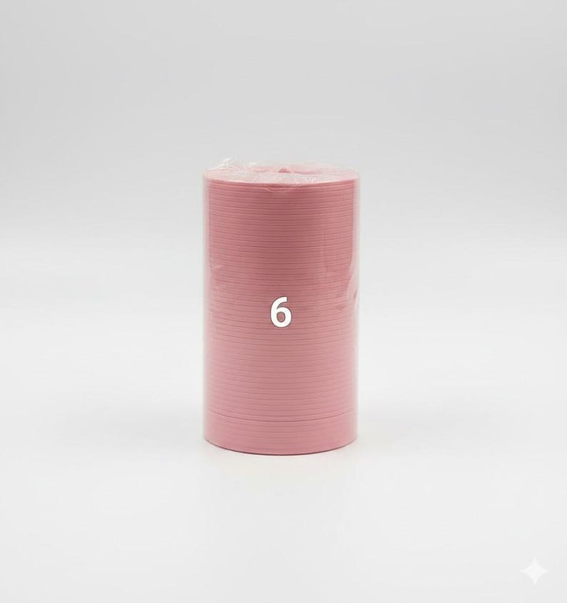 K&ouml;nnte beinhalten: Ein Stapel rosa Pappteller, verpackt in klarem Kunststoff. Die Zahl "6" ist auf die Seite des Stapels gedruckt. Die Teller haben eine einfarbige, hellrosa Farbe.