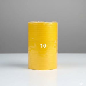 K&ouml;nnte beinhalten: Ein leuchtend gelbes, zylindrisches Objekt mit der Zahl "10" auf der Vorderseite. Das Objekt hat eine geriffelte Textur und scheint in klarem Kunststoff verpackt zu sein. Der Hintergrund ist ein Grau-Wei&szlig;-Verlauf.