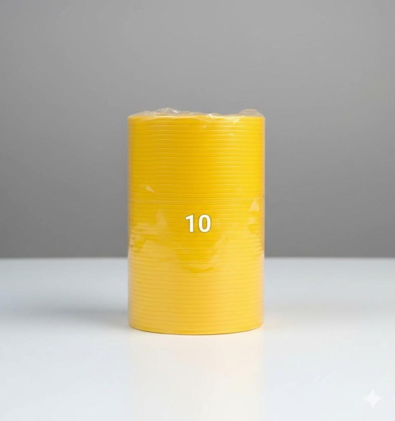 K&ouml;nnte beinhalten: Ein leuchtend gelbes, zylindrisches Objekt mit der Zahl "10" auf der Vorderseite. Das Objekt hat eine geriffelte Textur und scheint in klarem Kunststoff verpackt zu sein. Der Hintergrund ist ein Grau-Wei&szlig;-Verlauf.