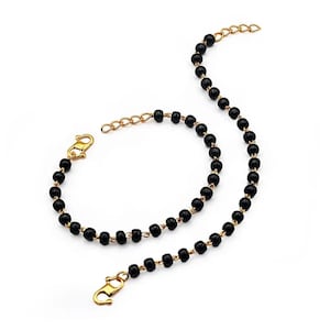 May include: A gold-toned necklace and bracelet set featuring black beads. The necklace and bracelet have a delicate chain design and are connected with gold-colored clasps. The jewelry is displayed on a white background.