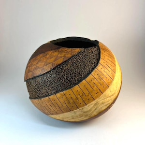 May include: A handcrafted, spherical decorative vessel with a dark interior. The exterior features a mix of textures and colors, including light brown, dark brown, and a woven, net-like pattern. The vessel is approximately 8 inches in diameter.