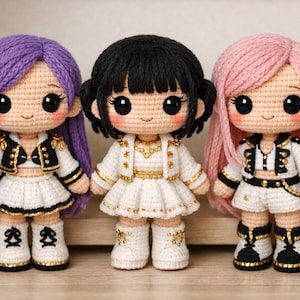 Puede incluir: Tres muñecas de ganchillo hechas a mano con pelo morado, negro y rosa. Cada muñeca viste un atuendo blanco con detalles dorados y negros, incluyendo una chaqueta, falda o pantalón corto y botas. Las muñecas tienen ojos grandes y expresivos.