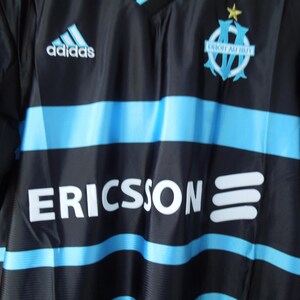 May include: Black and blue soccer jersey with horizontal light blue stripes. Features the Adidas logo, team emblem, and the word "ERICSSON" in white. The jersey has a V-neck design.