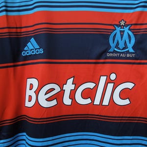 May include: Red and blue striped jersey with the Adidas logo and the text "Betclic". The jersey also features a team emblem and the text "Droit au But".