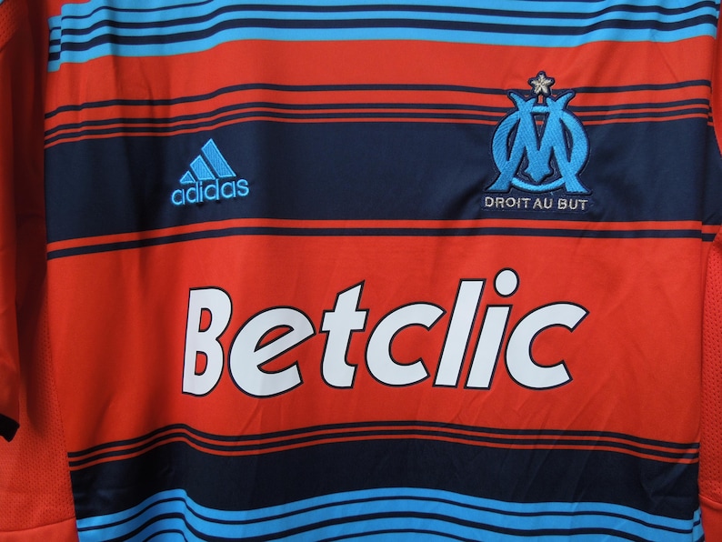 May include: Red and blue striped jersey with the Adidas logo and the text "Betclic". The jersey also features a team emblem and the text "Droit au But".