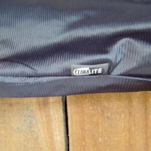 May include: Close-up of a dark navy blue fabric with a textured, ribbed pattern. The fabric has a slight sheen and a tag that reads "CLIMALITE" in white lettering.