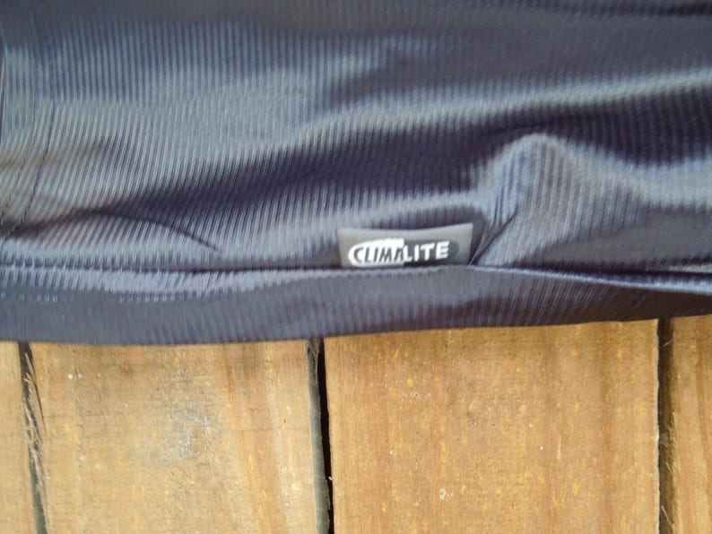May include: Close-up of a dark navy blue fabric with a textured, ribbed pattern. The fabric has a slight sheen and a tag that reads "CLIMALITE" in white lettering.