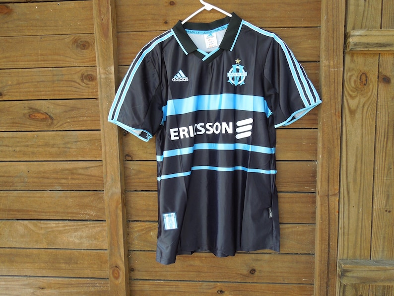May include: Black and blue Adidas soccer jersey with the word "ERISSON" across the front. The jersey has light blue stripes and accents, a collar, and the Adidas logo. The team logo is on the chest.
