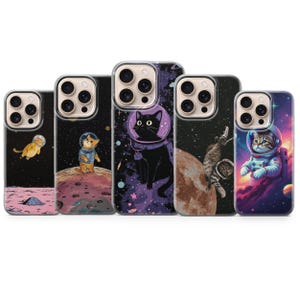 May include: Five phone cases with space-themed cat designs. Each case features a different cat astronaut illustration against a backdrop of planets, stars, and nebulae. The cats are depicted in spacesuits and helmets, exploring the cosmos.
