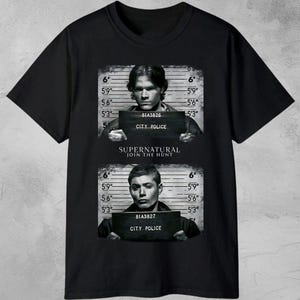 以下が含まれることがあります： 2 人の男性の顔写真風の画像がプリントされた黒いTシャツ。身長の測定値が示されています。「SUPERNATURAL JOIN THE HUNT」の文字が画像間に配置されています。「DIGITAL DOWNLOAD」の文字が上部にあります。