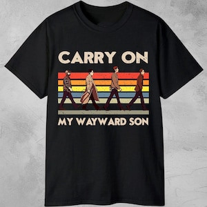 Pode incluir: Camiseta preta com o texto "DIGITAL DOWNLOAD" no topo. A camiseta apresenta as palavras "CARRY ON MY WAYWARD SON" com um gráfico de quatro figuras caminhando sobre um fundo listrado.