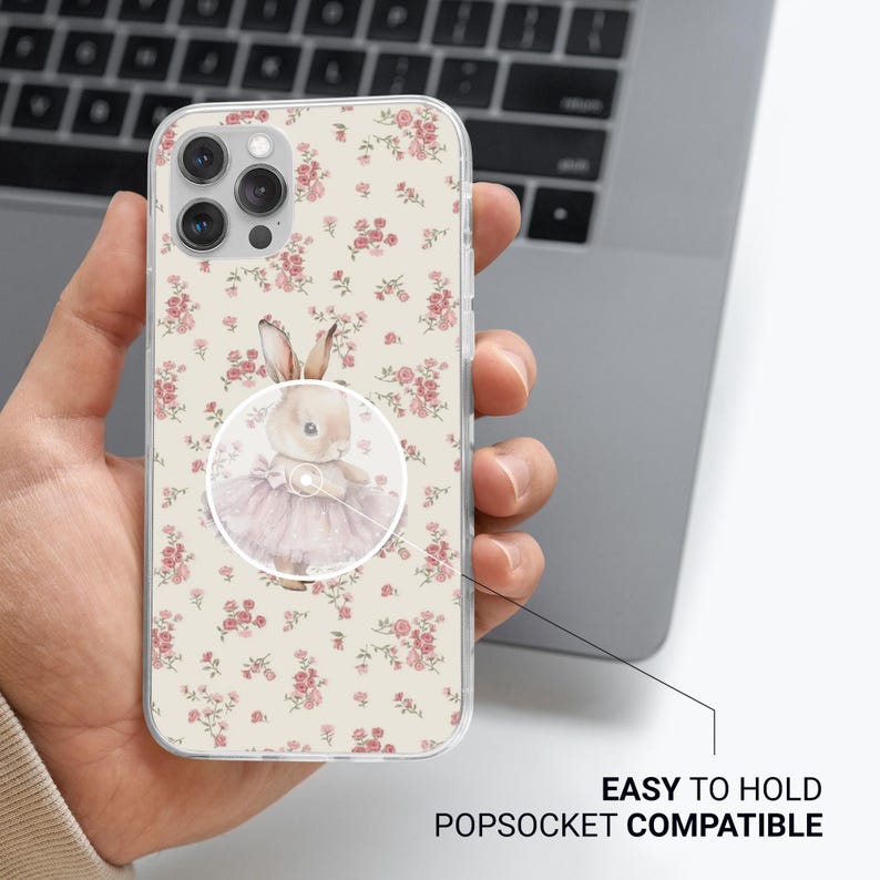 May include: Clear phone case with a floral pattern of pink roses on a cream background. A PopSocket with a watercolor illustration of a bunny wearing a pink tutu is attached. The text "EASY TO HOLD POPSOCKET COMPATIBLE" is visible.