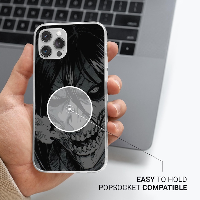 May include: A clear phone case featuring a black and gray illustration of a character with sharp teeth and intense eyes. The text "EASY TO HOLD POPSOCKET COMPATIBLE" is visible. The phone case is held in a hand.