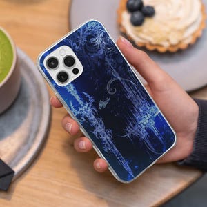 May include: A clear phone case with a dark blue design featuring a sword, butterfly, and ornate patterns. The case is held in a hand, showcasing the phone's camera and overall design.