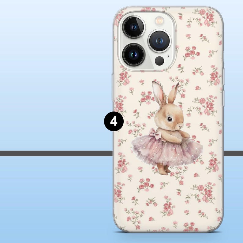 May include: A clear phone case featuring a watercolor illustration of a bunny wearing a pink tutu. The case has a floral pattern of pink roses on a cream background. The phone's camera lenses are visible.