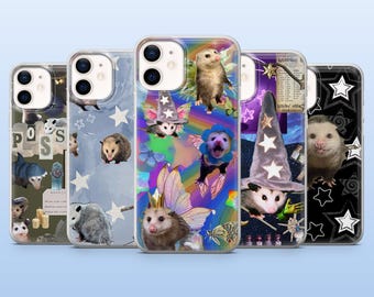 May include: Five smartphone cases featuring various opossum designs. The cases display opossums with wizard hats, fairy wings, and star patterns against backgrounds of rainbows, dark skies, and collage-style graphics with text and candles.