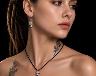 Puede incluir: Un colgante de calavera en tono plateado que cuelga de un fino cordón negro, junto con un pendiente de calavera a juego. La joyería de calavera presenta rasgos faciales detallados, incluyendo cuencas oculares, nariz y dientes.