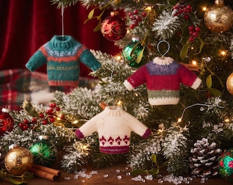 May include: Three miniature knitted sweater ornaments hanging on a Christmas tree. One sweater is teal with orange stripes, one is maroon and purple with a cream hem, and one is cream with a maroon geometric pattern at the bottom hem.
