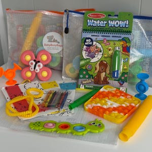 May include: A collection of colorful children's toys, including a butterfly-shaped toy, a water-reveal activity book, and a pop-it toy. The toys are arranged on a white surface, with some items inside clear mesh bags. The color palette includes orange, pink, yellow, and green.