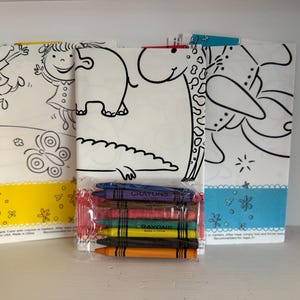 May include: Three coloring book pages with black line drawings of a girl, butterfly, elephant, giraffe, and flowers. A package of crayons in various colors sits in front of the pages. The pages have yellow and blue borders.