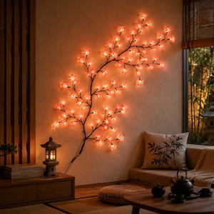 Puede incluir: Una rama de cerezo con luces LED montada en la pared, que presenta numerosas bombillas de color naranja rojizo con forma de flor unidas a tallos oscuros y delgados que se extienden para crear un efecto de iluminación cálida.