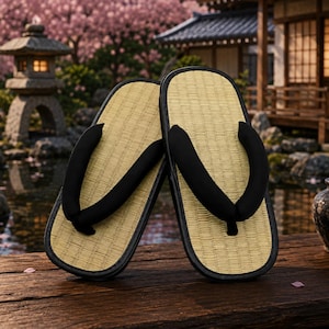 Puede incluir: Un par de sandalias japonesas tradicionales con una plantilla de paja tejida y correas de tela negra gruesa. Las sandalias tienen una forma rectangular redondeada con un borde negro, diseñadas para calzarse fácilmente con un estilo clásico.