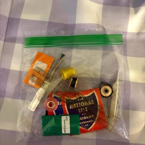 May include: A clear plastic bag containing sewing supplies including a small clear ruler with markings in inches, a yellow thimble, a black spool of thread, a metal seam ripper, a pair of tweezers, a pink button, and a vintage National Life insurance card.