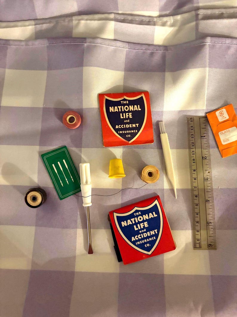 May include: A collection of sewing notions including two red matchbooks labeled The National Life and Accident Insurance Co., a green needle case, a yellow thimble, spools of thread, a white seam ripper, and a 6-inch metal ruler.