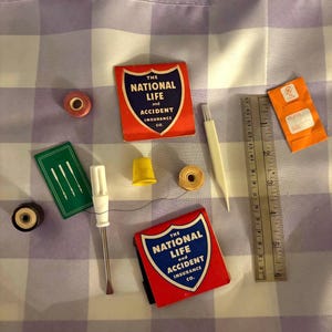 May include: A collection of sewing notions including two red matchbooks labeled The National Life and Accident Insurance Co., a yellow thimble, a white seam ripper, a green needle packet, spools of thread, and a 6-inch metal ruler.