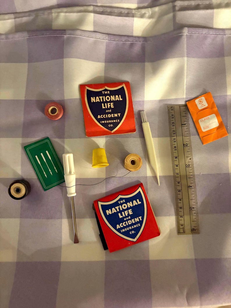 May include: A collection of sewing notions including two red matchbooks labeled The National Life and Accident Insurance Co., a yellow thimble, a white seam ripper, a green needle packet, spools of thread, and a 6-inch metal ruler.