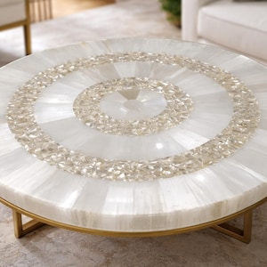 May include: Round white coffee table with a decorative crystal and stone inlay design. The table has a gold metal base and legs. The tabletop features a circular pattern of crystals and white stone segments.