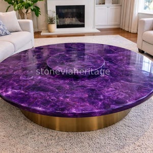May include: A circular coffee table with a vibrant purple marble top and a gold-coloured base. The table features a central, smaller circular inset. The table is in a living room setting.