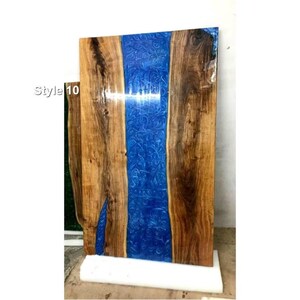 May include: A rectangular wooden table top with a blue resin river design. The wood has a natural grain and a dark brown color. The blue resin has a swirling pattern. The text "Style 10" is visible on the left side.