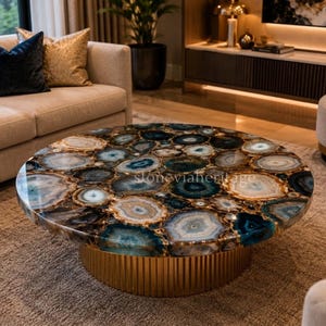 May include: A circular coffee table featuring a polished agate stone top in shades of blue, brown, and white. The table has a gold-coloured, ribbed base. A striking centrepiece for a living room.