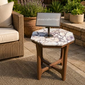 May include: A hexagonal side table with a white and purple marble top and a dark brown wooden base. A rectangular metal sign with a stand is placed on the table surface, featuring the text stoneviaheritage printed in white on a silver background.